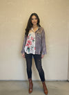 Model wearing a brown plaid mixed-print button-up blouse with floral and leopard accents, paired with dark skinny jeans and brown patent ankle boots in a boutique setting.