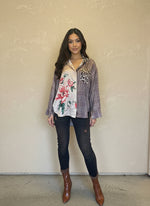 Model wearing a brown plaid mixed-print button-up blouse with floral and leopard accents, paired with dark skinny jeans and brown patent ankle boots in a boutique setting.