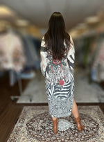 Back view of woman wearing celestial and floral print maxi dress with zebra pattern and “Blessed” script detail, styled with brown boots.