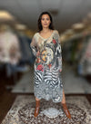 Woman posing in long boho-inspired maxi dress featuring artistic sun and moon graphic, red floral accents, and zebra pattern, styled with brown ankle boots.