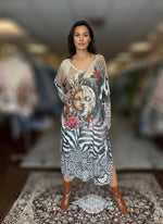 Woman posing in long boho-inspired maxi dress featuring artistic sun and moon graphic, red floral accents, and zebra pattern, styled with brown ankle boots.