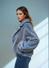 Side view of a woman in a soft blue ribbed faux fur jacket with folded collar and oversized sleeves, paired with casual blue jeans.