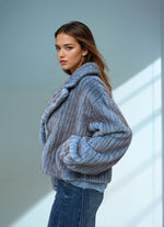Side view of a woman in a soft blue ribbed faux fur jacket with folded collar and oversized sleeves, paired with casual blue jeans.