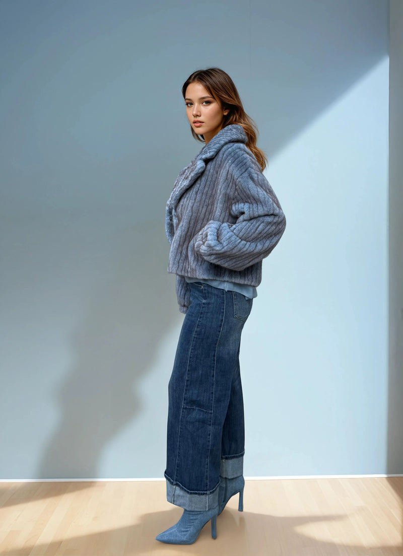 Full body view of a model in a blue ribbed faux fur short coat, styled with wide-leg cuffed jeans and pointed blue boots in natural light.