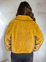 Back view of mustard yellow faux fur jacket highlighting ribbed texture and wide collar, modeled indoors with natural lighting