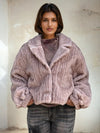 Model wearing a mauve-pink ribbed faux fur jacket with oversized sleeves and lapel collar, styled with gray washed jeans.