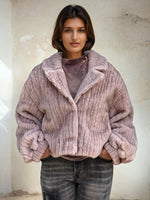 Model wearing a mauve-pink ribbed faux fur jacket with oversized sleeves and lapel collar, styled with gray washed jeans.