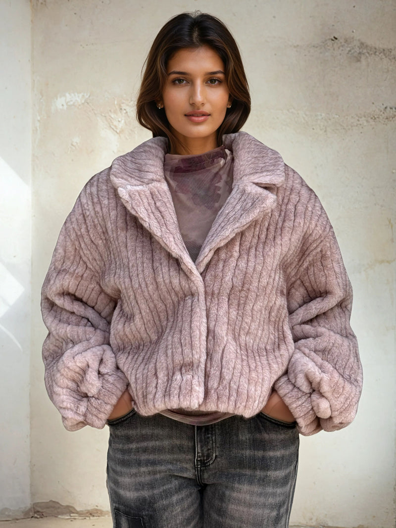 Model wearing a mauve-pink ribbed faux fur jacket with oversized sleeves and lapel collar, styled with gray washed jeans.