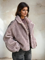 Side angle of a mauve ribbed faux fur short coat with structured collar and plush texture, paired with faded black jeans.