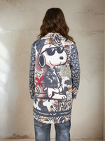 Back view of a woman in a statement jacket with a large Snoopy graphic, bold animal prints, and street-style patches, styled with gray jeans and heels.