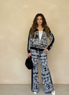 Front view of woman wearing matching black and white knit jacket and wide-leg pants set with leopard and foliage pattern, holding black handbag.