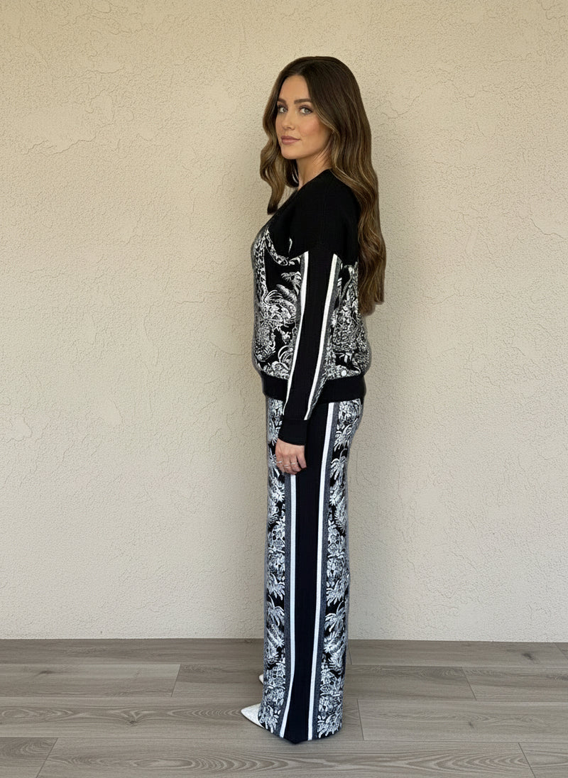 Side view of woman wearing black and white jacquard knit jacket and wide-leg pants with tropical and leopard print design.